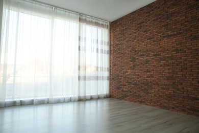 Empty room with red brick wall, large window and wooden floor