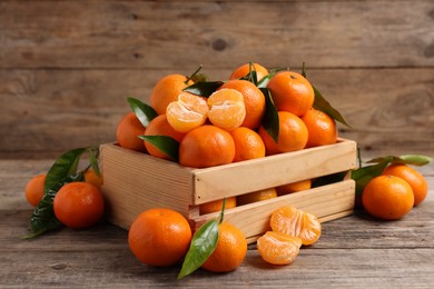 Photo of Delicious tangerines with leaves on wooden table