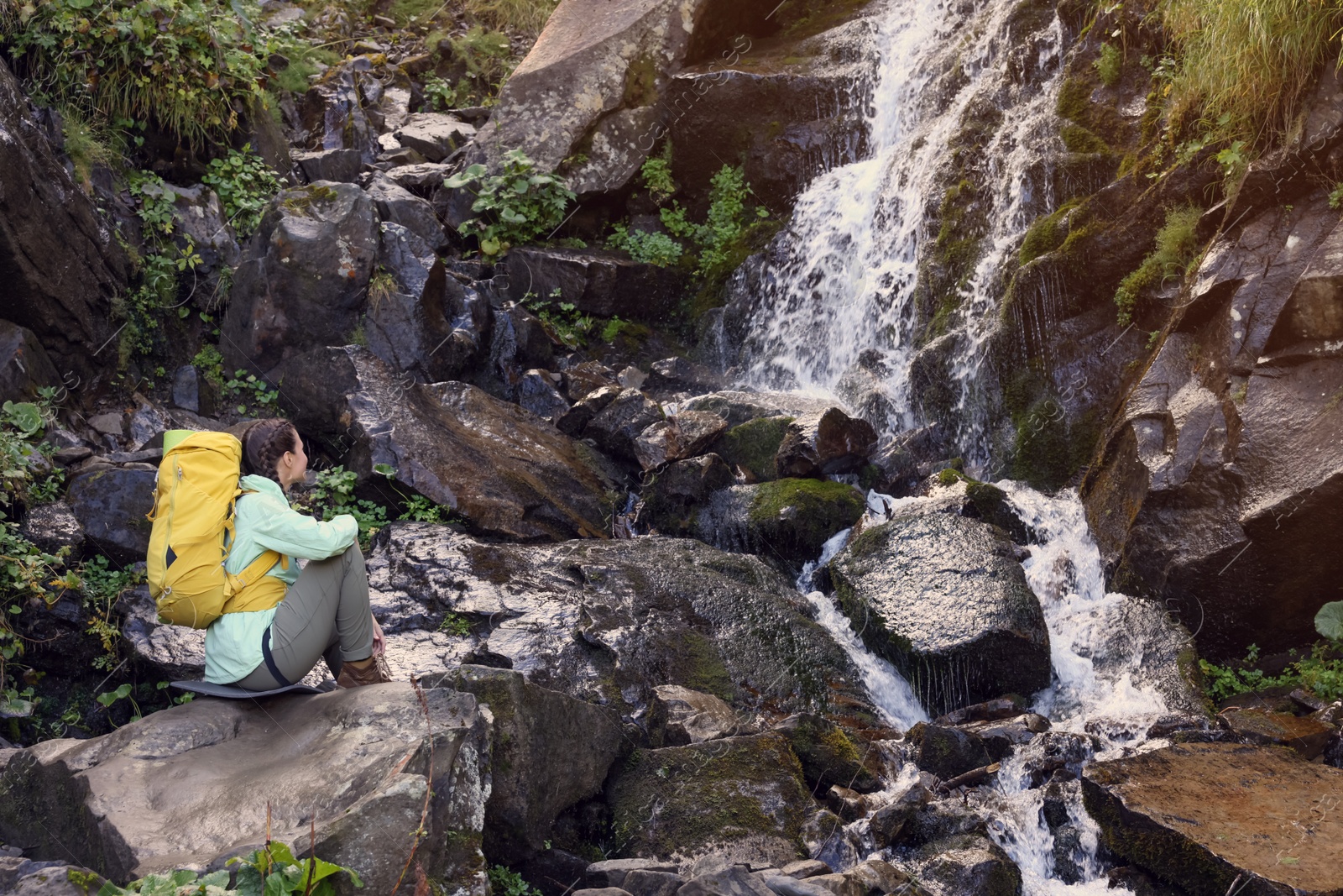 Photo of Tourist with backpack near waterfall in mountains. Space for text