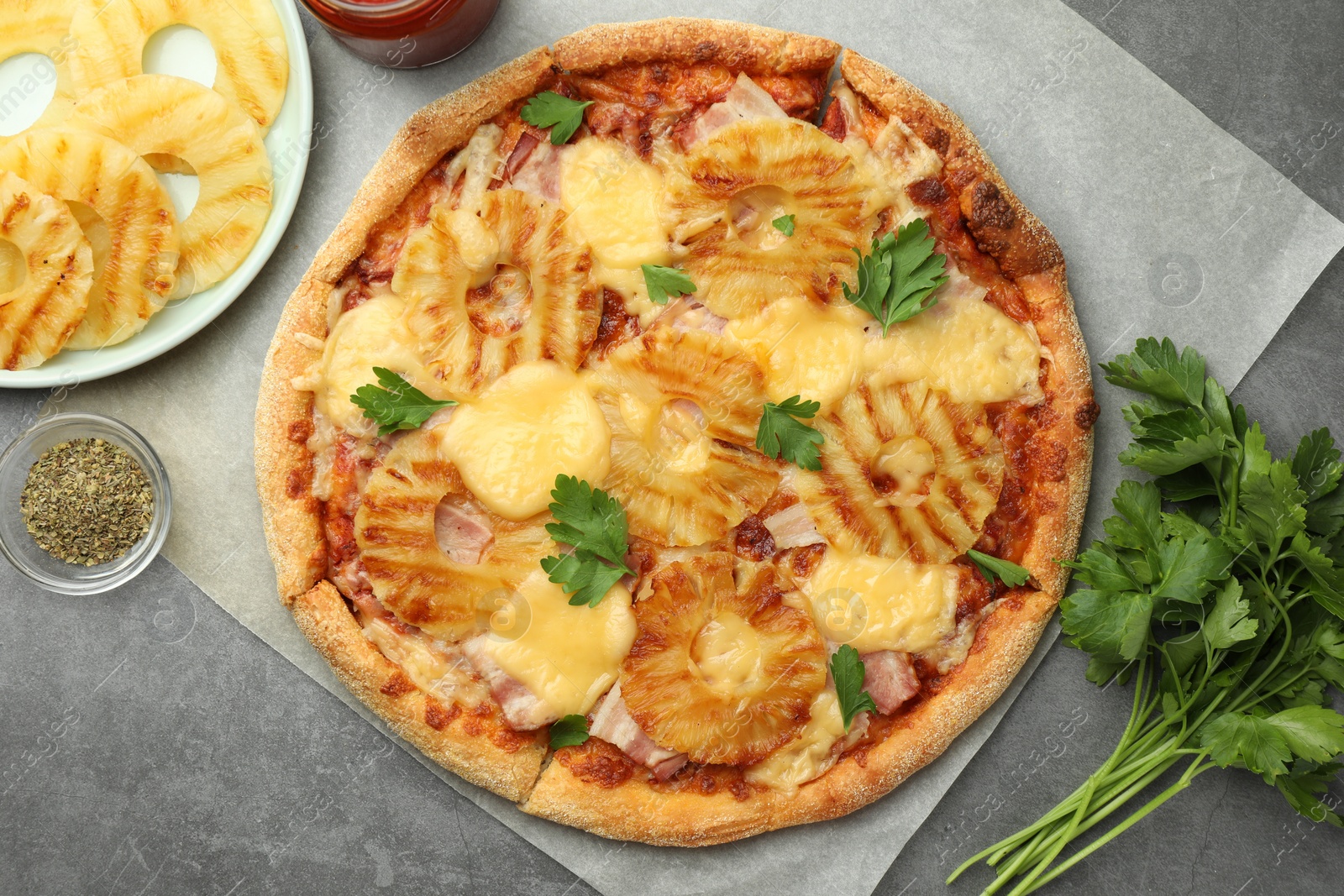 Photo of Delicious pineapple pizza and ingredients on gray table, flat lay