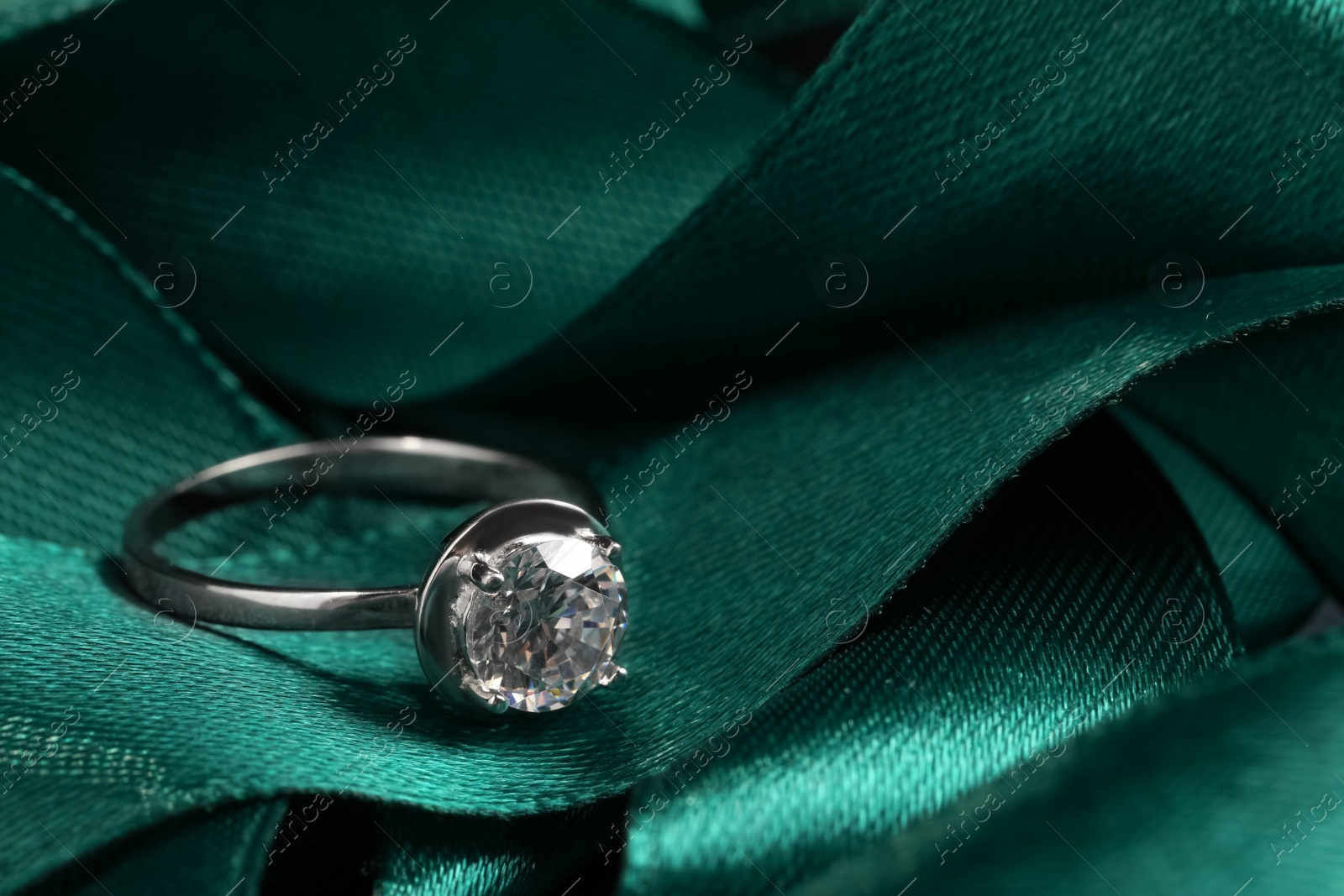 Photo of Beautiful luxury engagement ring with gemstone on green ribbon, closeup