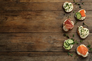 Delicious sandwiches with cream cheese and other ingredients on wooden table, flat lay. Space for text