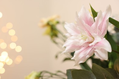 Beautiful lily flower against beige background with blurred lights, closeup. Space for text