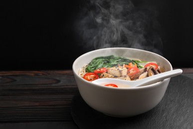 Image of Bowl of hot vegetarian ramen and spoon on dark wooden table, space for text