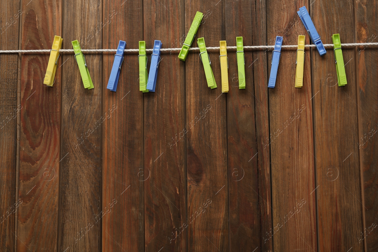 Photo of Colorful plastic clothespins and rope on wooden background, top view. Space for text