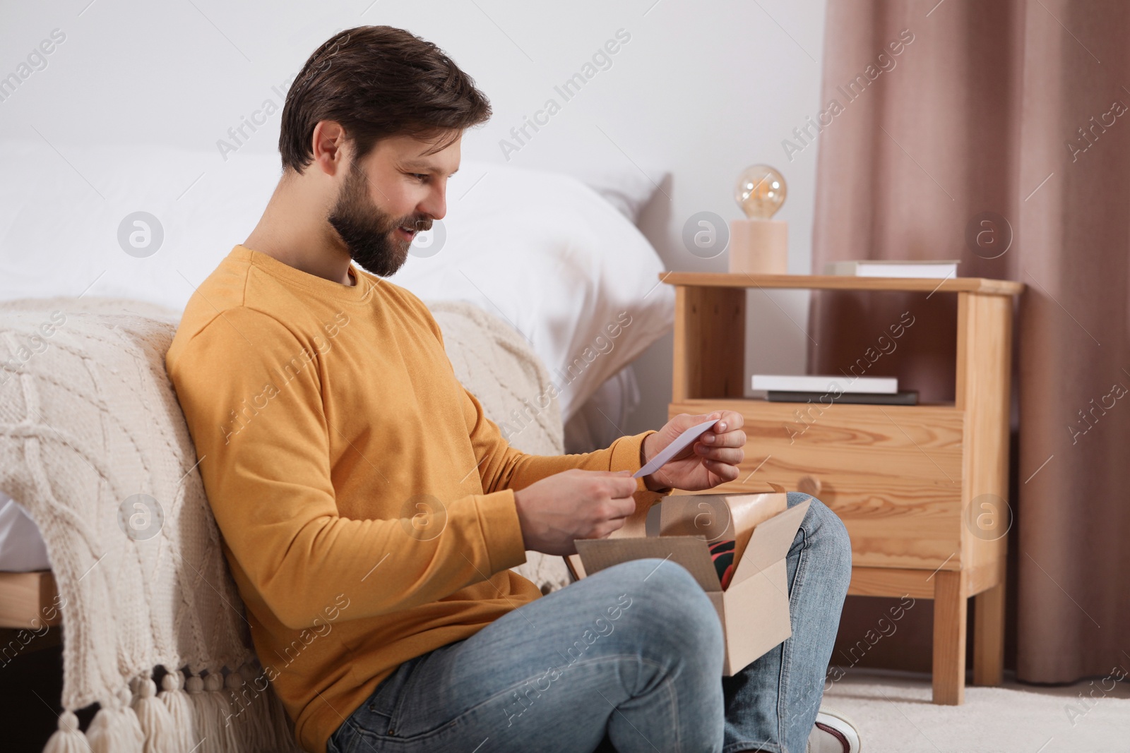 Photo of Happy man with greeting card near parcel at home. Internet shopping