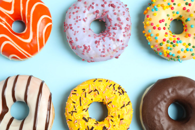 Photo of Delicious glazed donuts on light blue background, flat lay