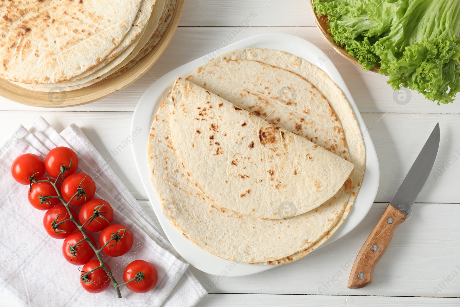 Photo of Tasty homemade tortillas, tomatoes, lettuce and knife on white wooden table, top view