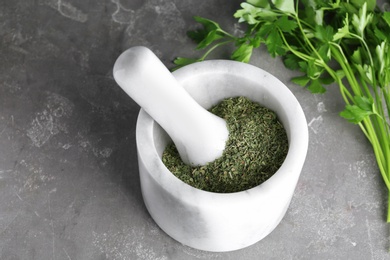 Photo of Mortar with dry parsley on grey table