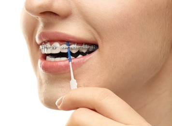 Photo of Woman with dental braces cleaning teeth using interdental brush on white background, closeup