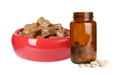 Wet pet food in feeding bowl and bottle with vitamin pills on white background