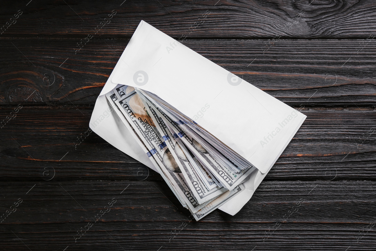 Photo of Envelope with dollar bills on black wooden table, top view. Bribe concept