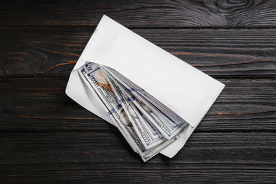 Photo of Envelope with dollar bills on black wooden table, top view. Bribe concept