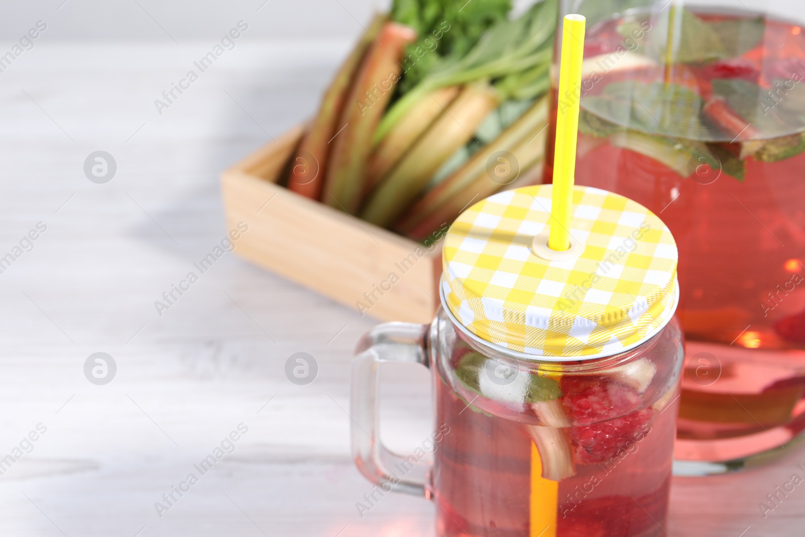 Photo of Mason jar of tasty rhubarb cocktail on white table, closeup. Space for text