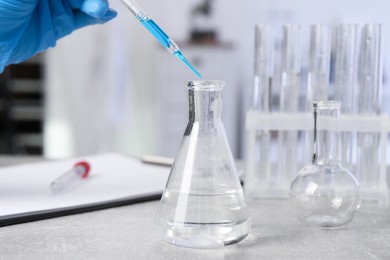 Photo of Laboratory analysis. Woman dripping liquid into flask at light grey table, closeup