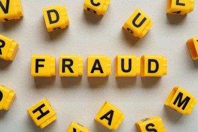 Word Fraud of yellow cubes with letters on light grey background, flat lay