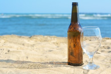 Photo of Bottle of beer and glass on sandy beach near sea. Space for text