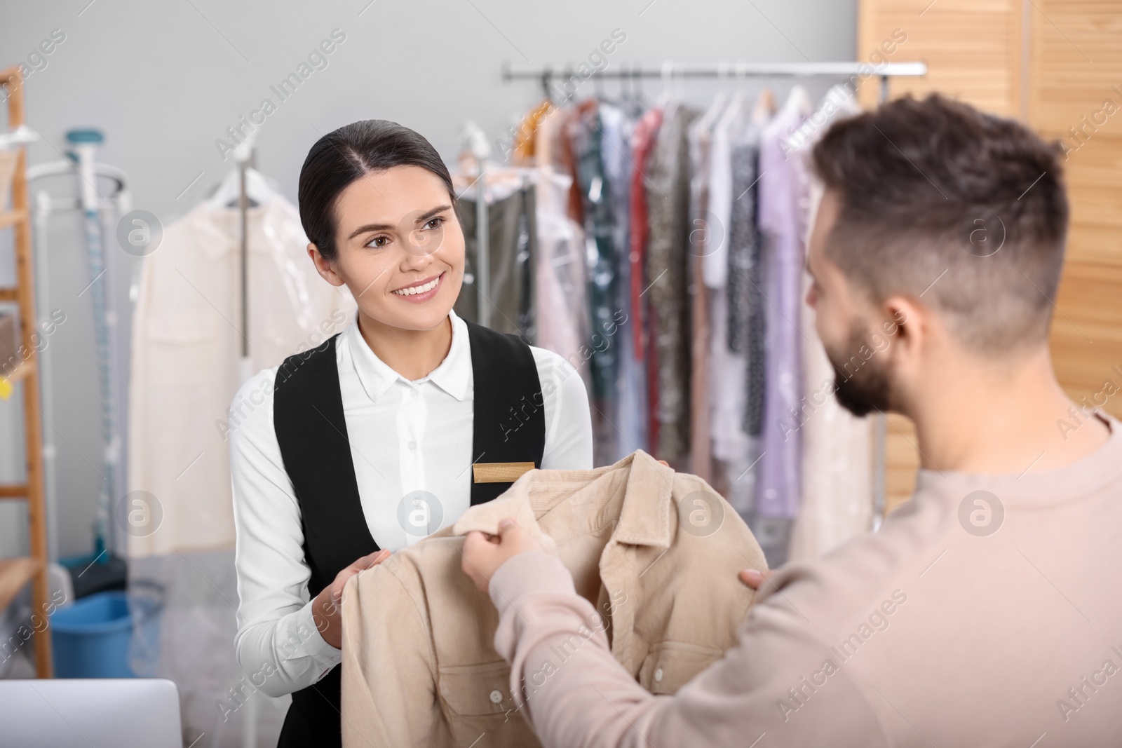 Photo of Dry-cleaning service. Happy worker receiving coat from client indoors