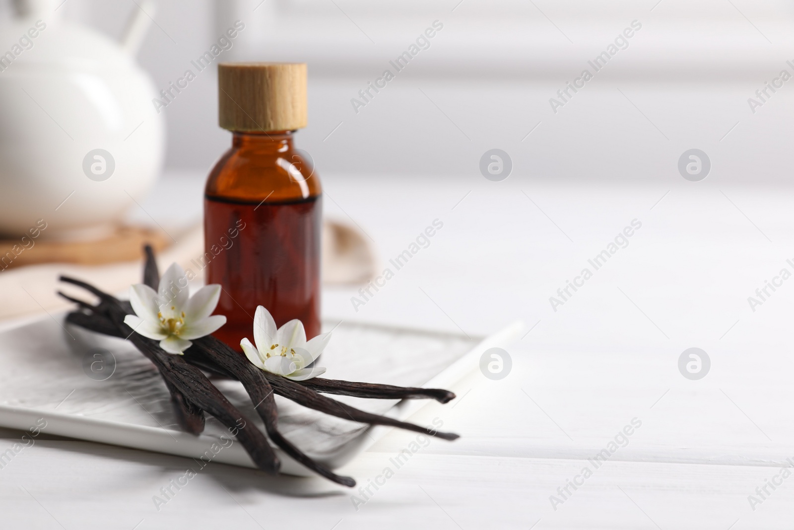 Photo of Vanilla pods, essential oil and flowers on white wooden table, space for text