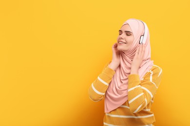Portrait of Muslim woman in hijab and headphones on orange background, space for text