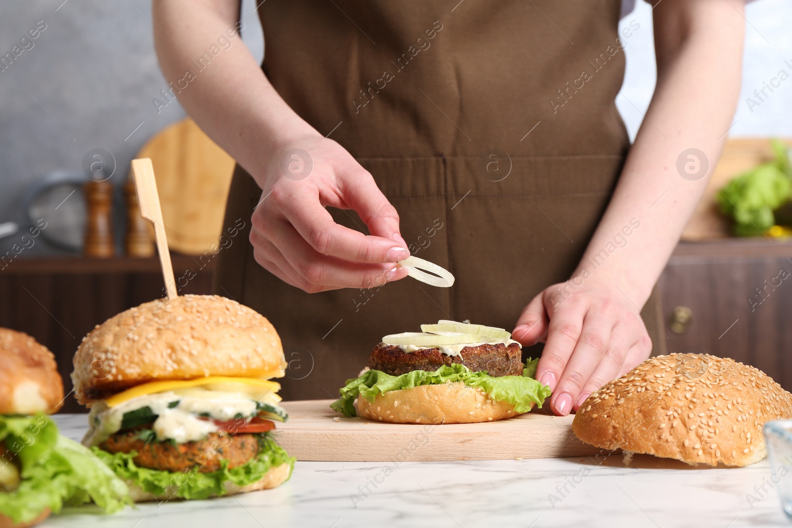 Photo of Woman making delicious vegetarian burger at white marble table, closeup