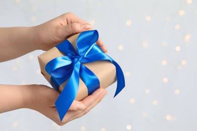Woman holding gift box with blue bow against blurred festive lights, closeup and space for text. Bokeh effect