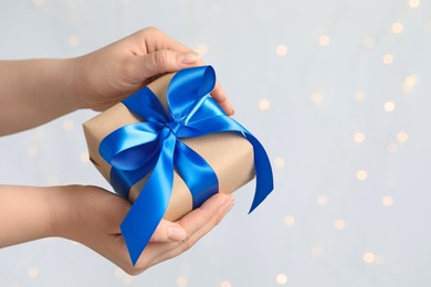 Photo of Woman holding gift box with blue bow against blurred festive lights, closeup and space for text. Bokeh effect