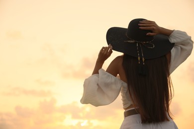 Photo of Young woman in hat at sunset, back view. Space for text