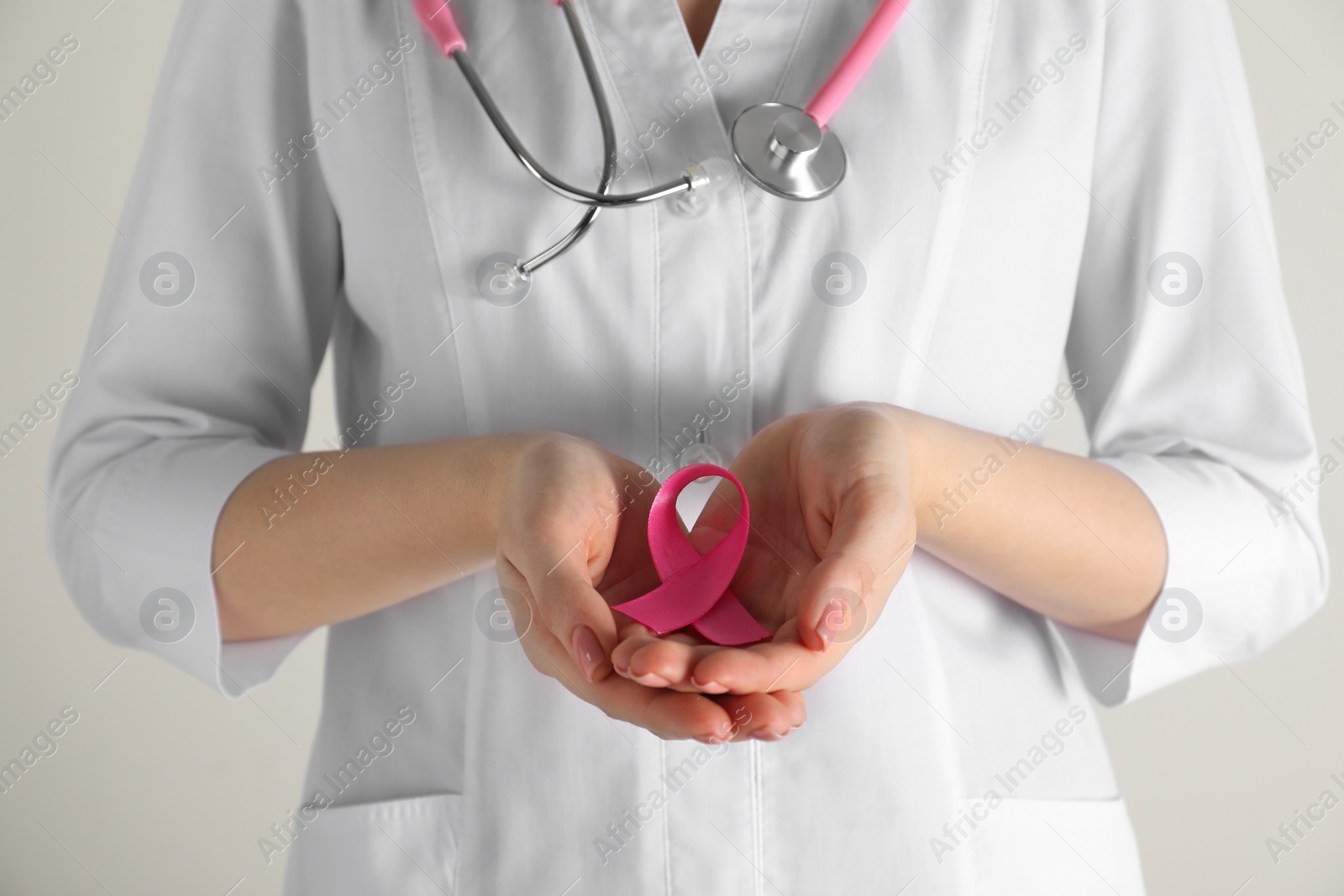 Photo of Mammologist with pink ribbon on light background, closeup. Breast cancer awareness