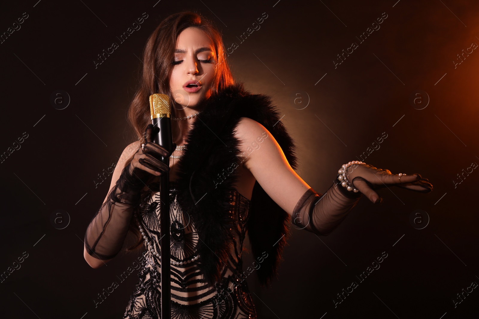 Photo of Beautiful young woman in stylish dress with microphone singing on dark background