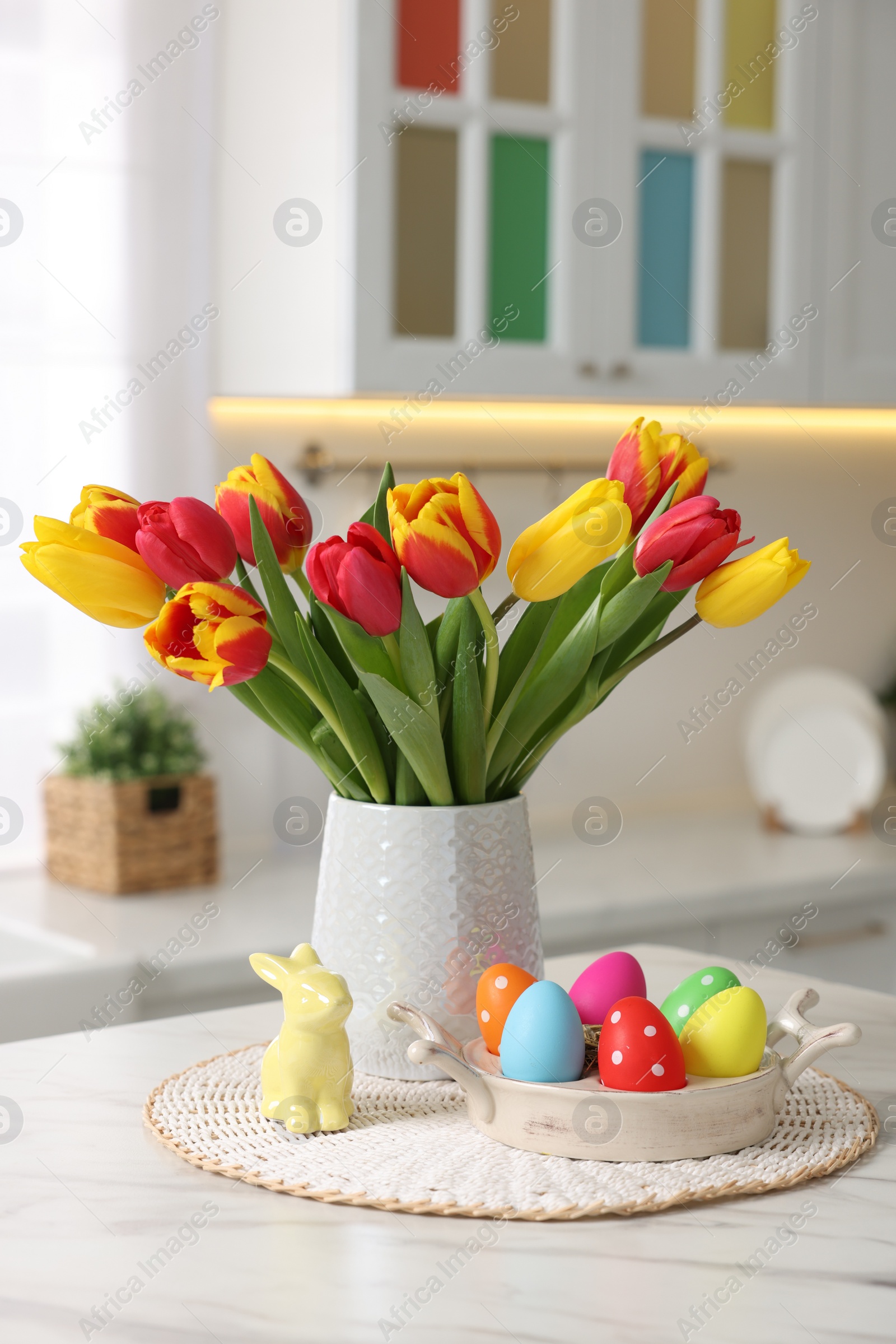 Photo of Easter decorations. Bouquet of tulips, painted eggs and bunny figure on table indoors