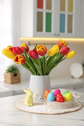 Photo of Easter decorations. Bouquet of tulips, painted eggs and bunny figure on table indoors