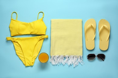 Photo of Beach towel, swimsuit, flip flops and sunglasses on light blue background, flat lay