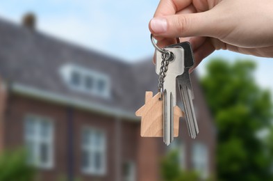 Image of Woman holding keys near house outdoors, closeup