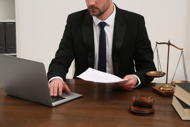 Photo of Law and justice. Lawyer working with documents and laptop at wooden table in office, closeup