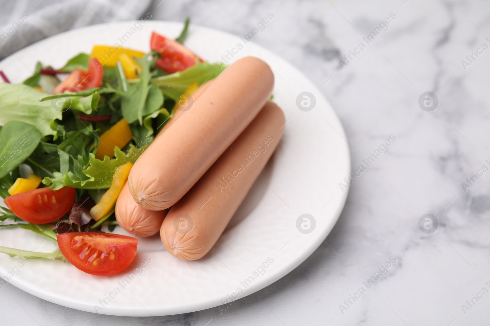 Photo of Delicious boiled sausages with salad on white marble table, closeup