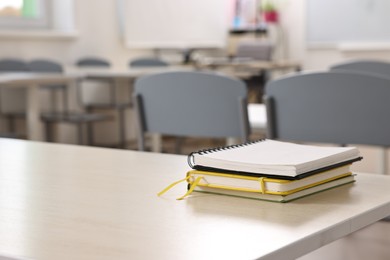 Photo of Stack of notebooks on wooden desk in empty classroom