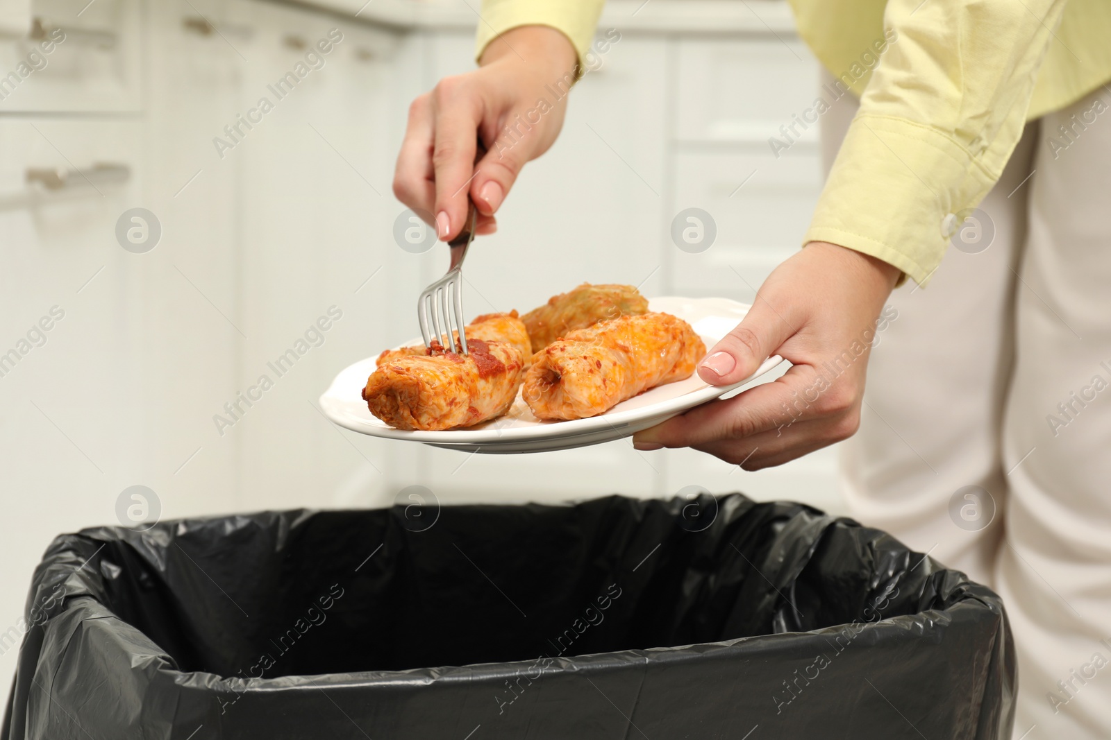 Photo of Woman throwing cabbage rolls into bin indoors, closeup