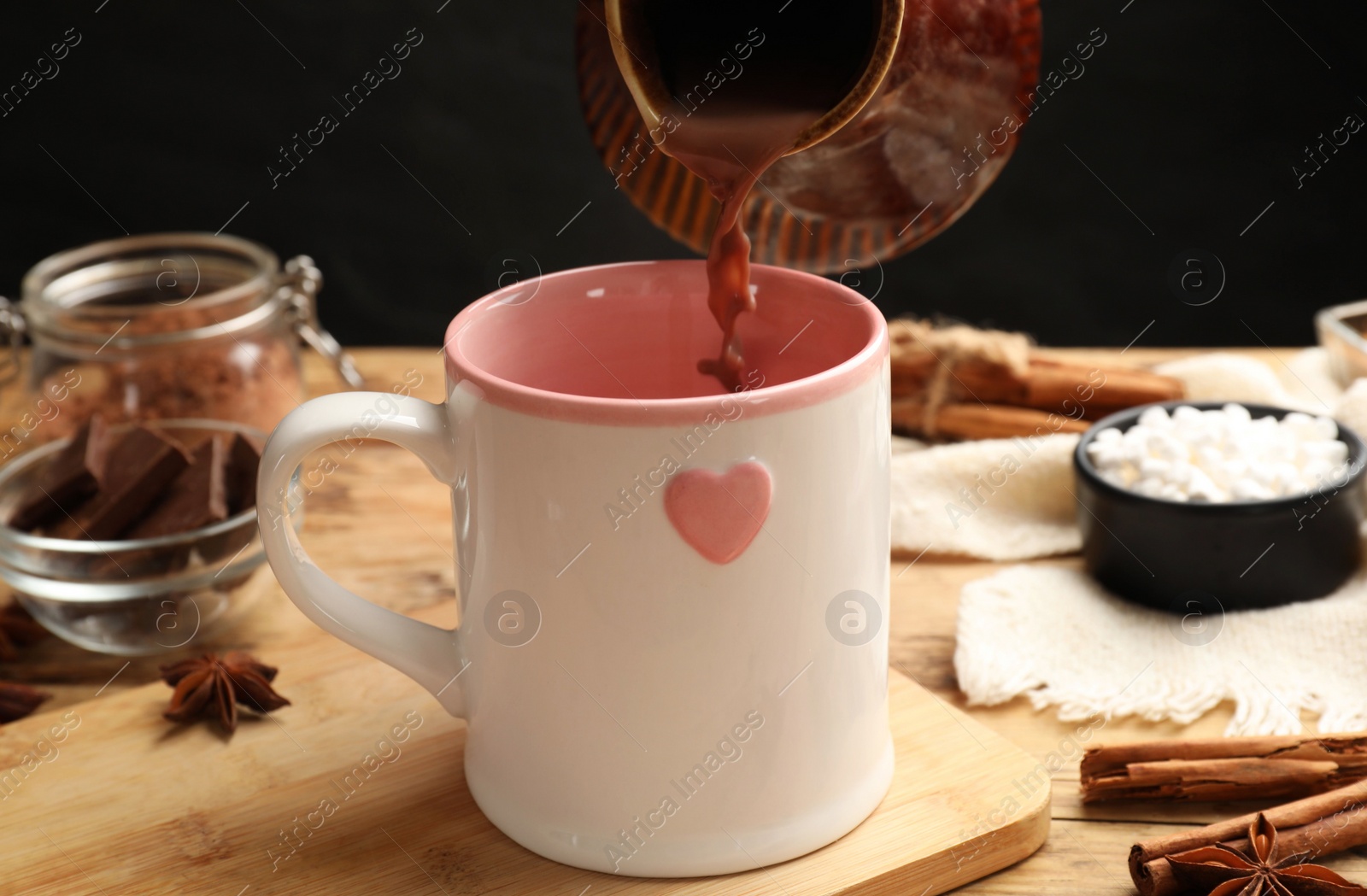 Photo of Pouring tasty hot chocolate into cup at wooden table, closeup