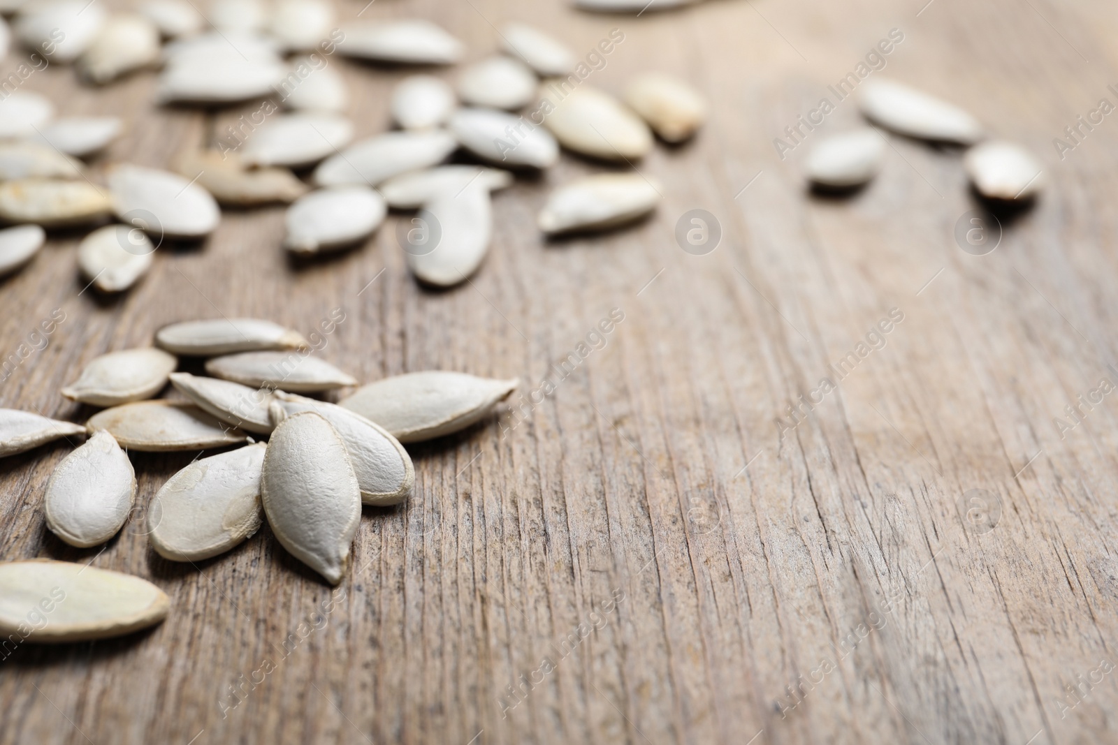 Photo of Closeup view of raw pumpkin seeds on wooden background, space for text. Vegetable planting