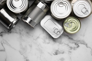 Many closed tin cans on white marble table, flat lay. Space for text