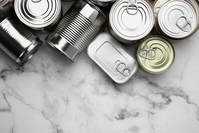 Photo of Many closed tin cans on white marble table, flat lay. Space for text