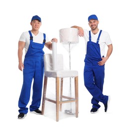 Workers near chair and lamp wrapped in stretch film on white background