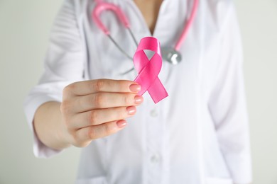 Photo of Mammologist with pink ribbon on light background, closeup. Breast cancer awareness
