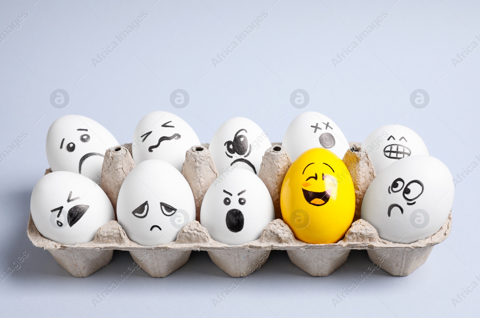 Photo of Yellow smiley egg among others with negative emotions in package on light background