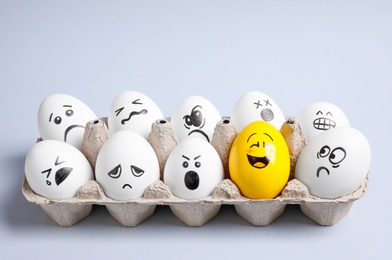 Photo of Yellow smiley egg among others with negative emotions in package on light background