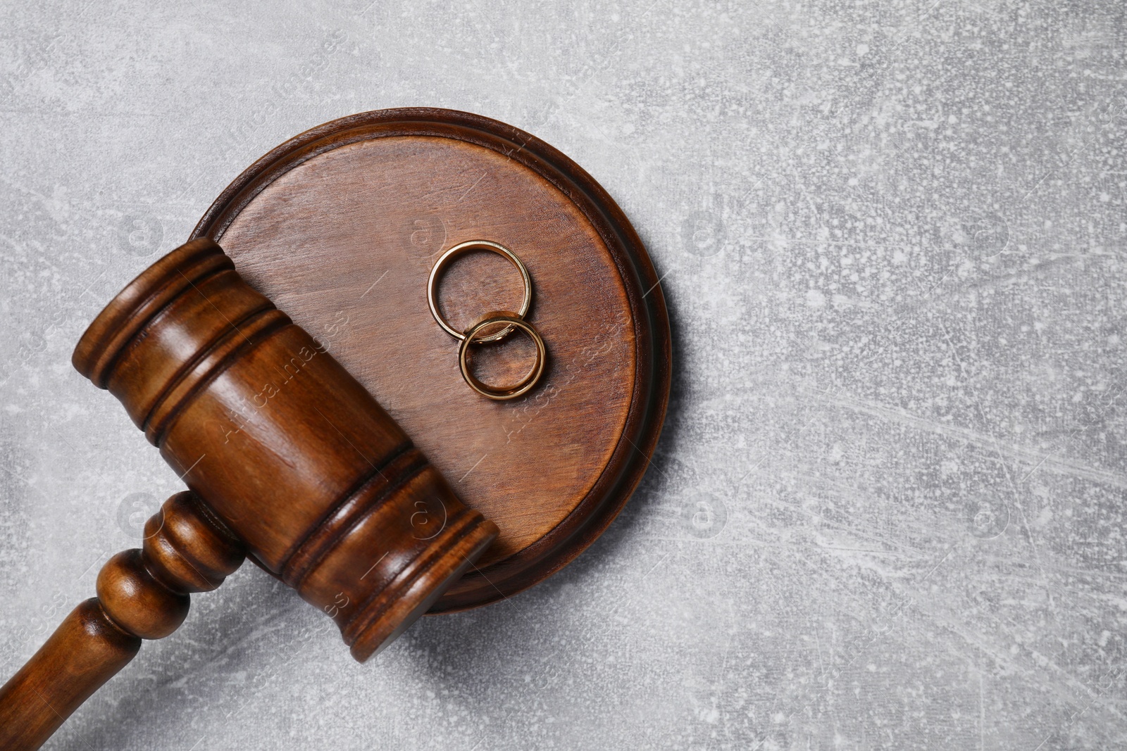 Photo of Divorce process. Wooden gavel and wedding rings on grey textured table, top view. Space for text