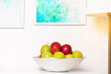 Photo of Bowl with different sweet apples on commode in room