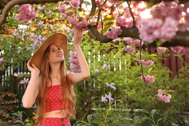 Photo of Beautiful teenage girl near blossoming sakura tree in park on sunny day, space for text