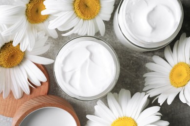 Photo of Jars of face cream and beautiful chamomiles on grey table, flat lay